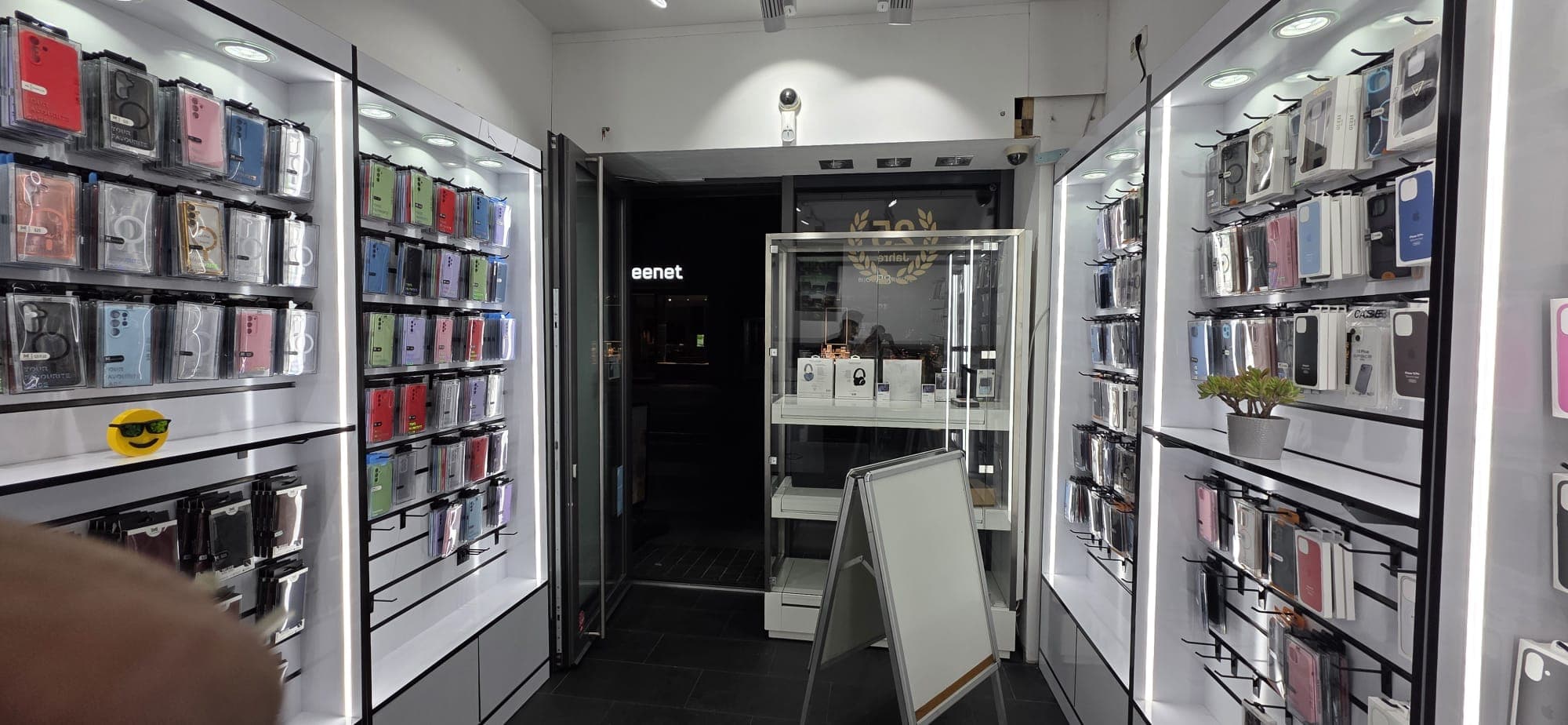 Panorama des Verkaufsraums: beidseitig beleuchtete Wände voller Handyhüllen und Zubehör, dazwischen eine Glasvitrine.