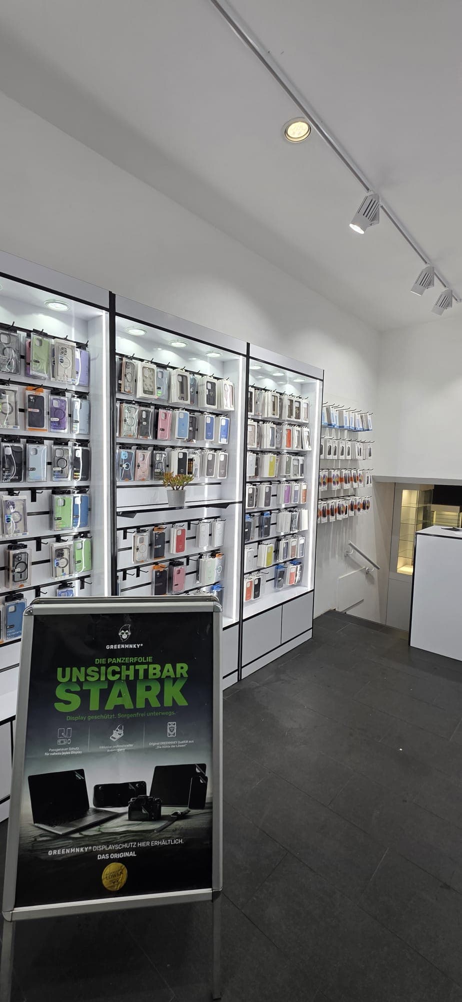Innenansicht des Ladens mit Displayschutz-Aufsteller und beleuchteten Regalen voller Zubehör.