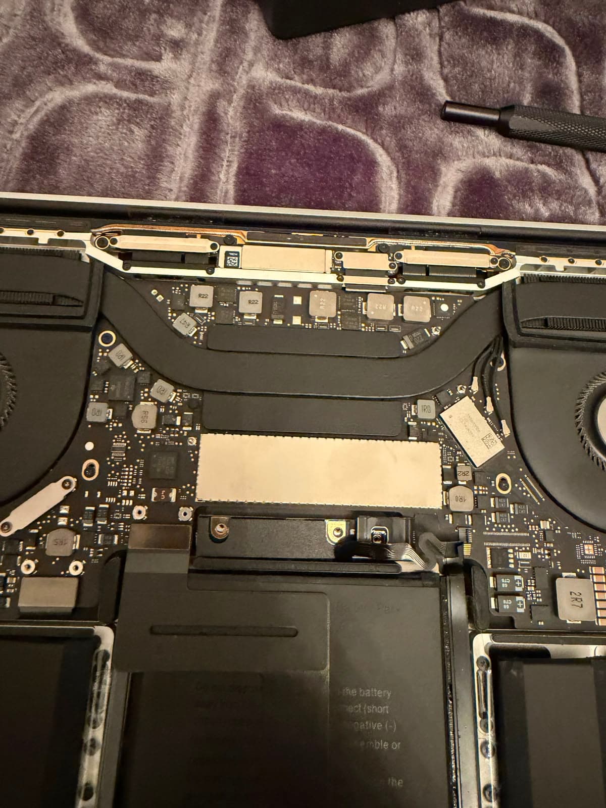 Geöffnetes MacBook auf der Werkbank: Logicboard, beide Lüfter und der Akku liegen frei, daneben ein Schraubendreher.