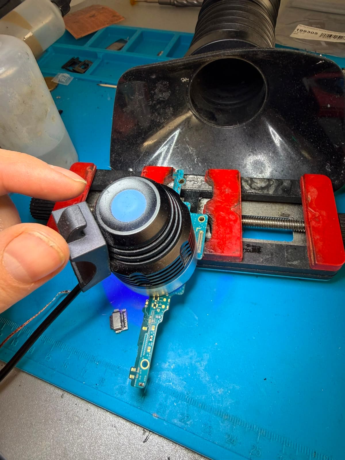 Eine Ladebuchsen-Platine ist in eine Werkstatt-Klemme gespannt und wird mit einer UV-Lampe ausgehärtet.