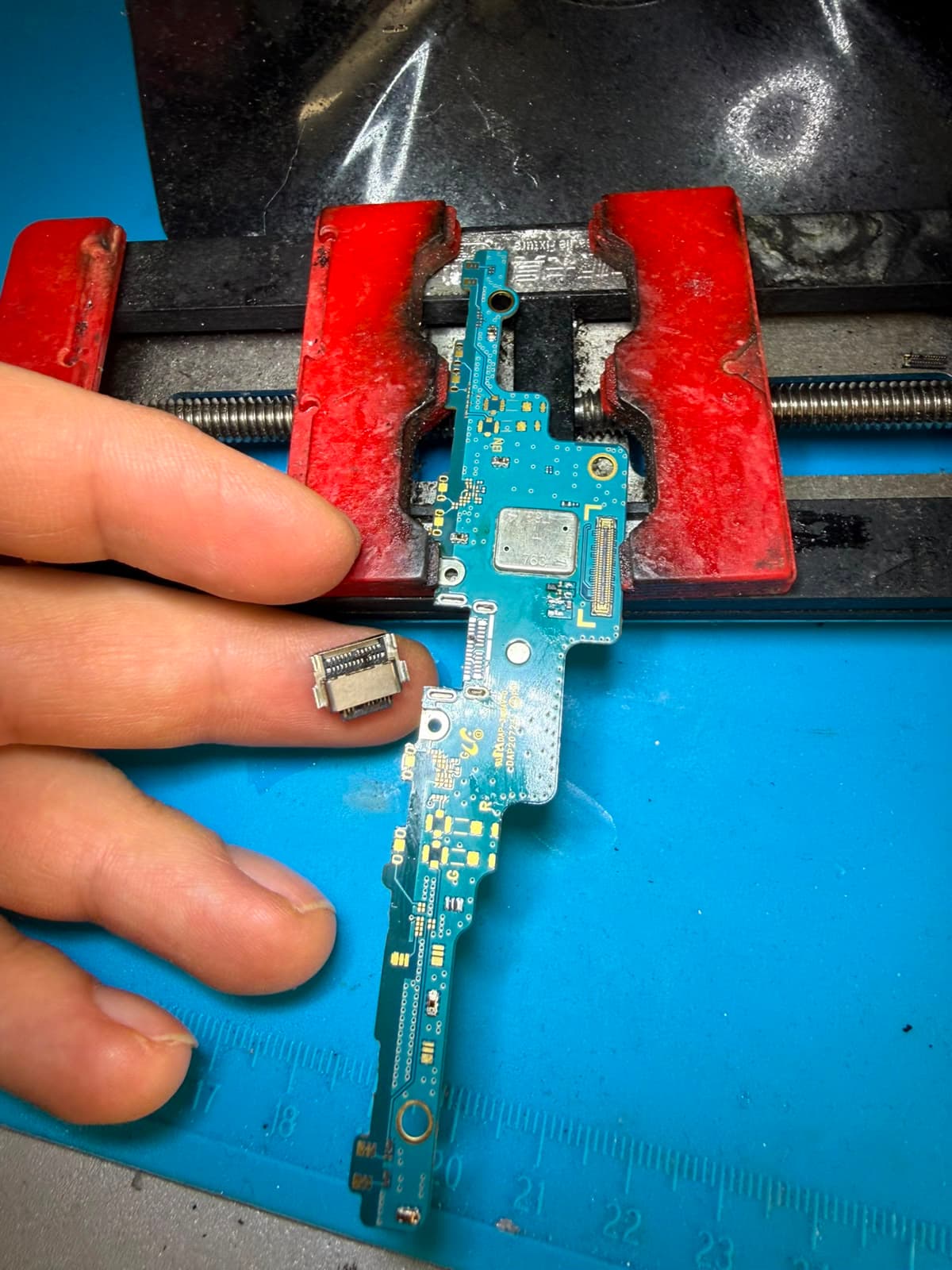 Ausgebaute Ladebuchsen-Platine eines Smartphones, daneben der abgelöste USB-C-Anschluss auf der Fingerspitze.